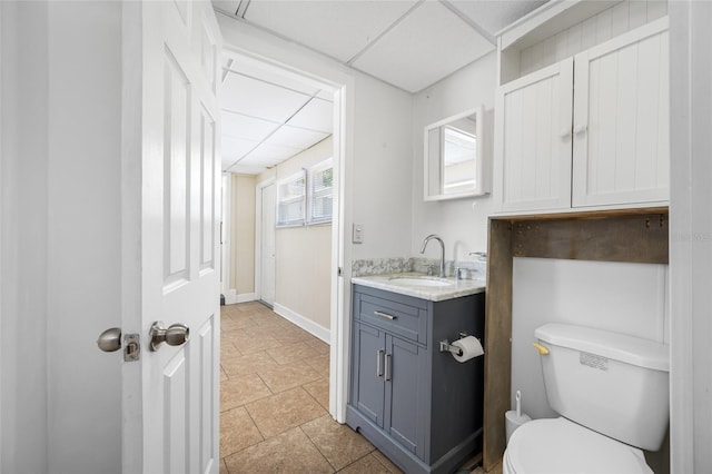 bathroom with vanity, baseboards, toilet, stone finish floor, and a paneled ceiling