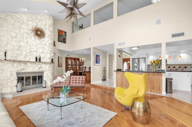 living area featuring a fireplace, a chandelier, light wood finished floors, baseboards, and a towering ceiling