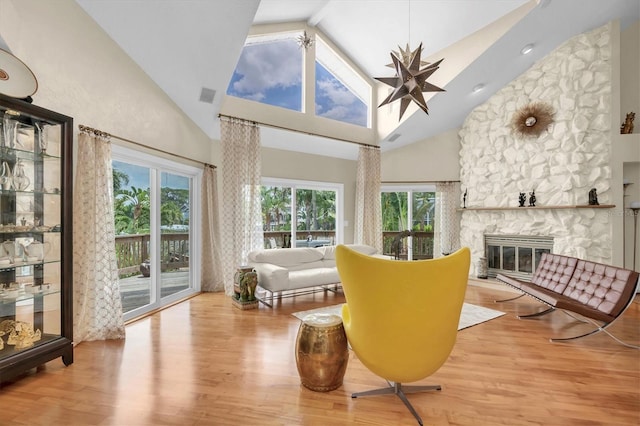 living area with high vaulted ceiling, plenty of natural light, wood finished floors, and a stone fireplace