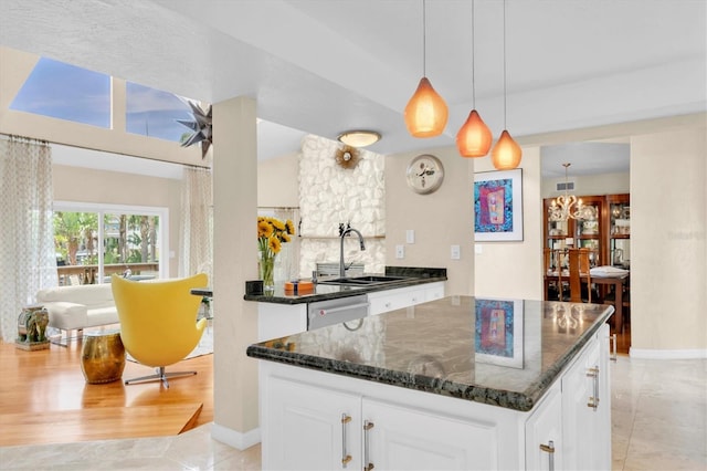 kitchen with a sink, white cabinets, stainless steel dishwasher, dark stone countertops, and baseboards