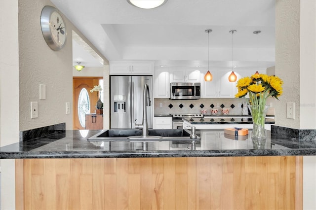 kitchen featuring appliances with stainless steel finishes, a textured wall, a peninsula, dark stone counters, and backsplash