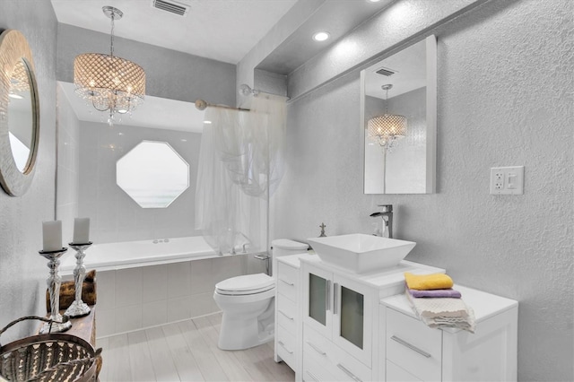 bathroom with a chandelier, a textured wall, tiled shower / bath, toilet, and vanity