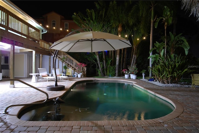 pool at night featuring a patio area, stairs, and an outdoor pool