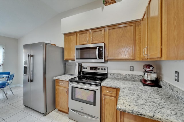 kitchen featuring stainless steel appliances, light stone countertops, vaulted ceiling, and light tile patterned floors
