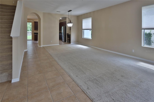 unfurnished living room featuring light carpet, baseboards, arched walkways, and light tile patterned floors