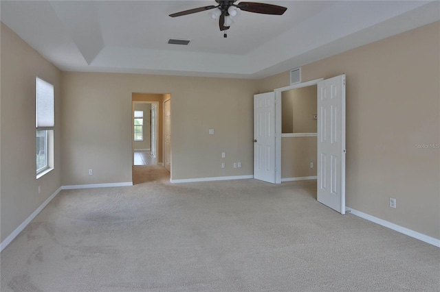 spare room featuring light colored carpet, ceiling fan, a tray ceiling, and visible vents
