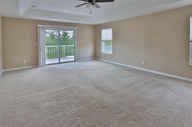 carpeted spare room featuring a wealth of natural light, a ceiling fan, a tray ceiling, and baseboards