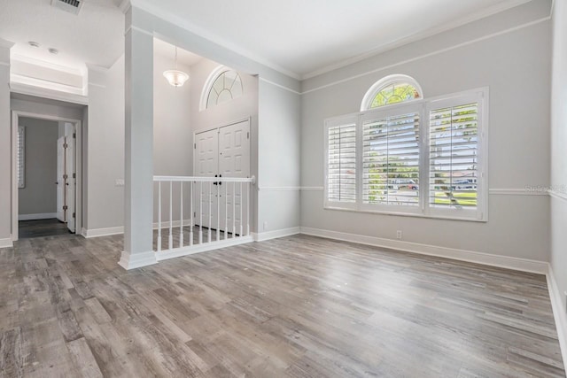 spare room with wood finished floors, visible vents, baseboards, and ornamental molding