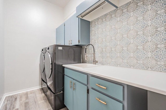clothes washing area featuring light wood-style flooring, a sink, baseboards, cabinet space, and washer and dryer