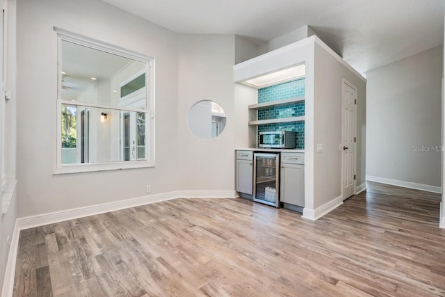 bar featuring beverage cooler, light wood finished floors, a dry bar, stainless steel microwave, and baseboards