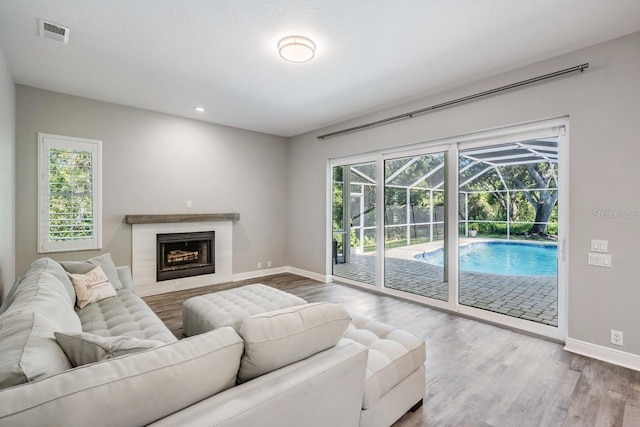 living area featuring baseboards, visible vents, wood finished floors, a sunroom, and a fireplace