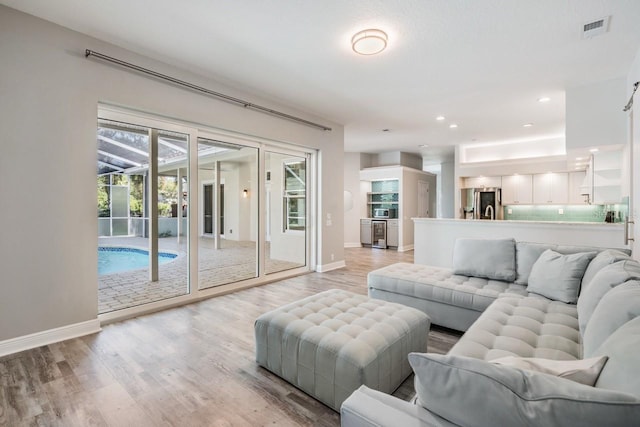 living area featuring baseboards, light wood-style floors, visible vents, and recessed lighting