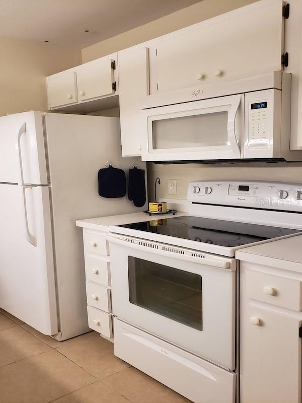 kitchen with white cabinets, light tile patterned floors, white appliances, and light countertops