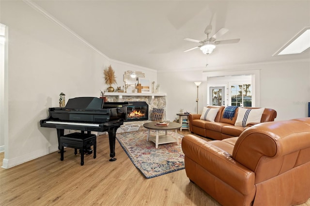 living area with light wood-type flooring, baseboards, ceiling fan, crown molding, and a stone fireplace