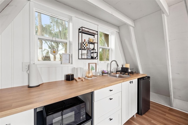 bar featuring black microwave, fridge, light wood-style flooring, and a sink