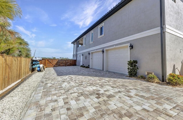 107 Sunset Dr, Nokomis, FL 34275 - view of side of home with a gate, fence, a garage, stucco siding, and decorative driveway