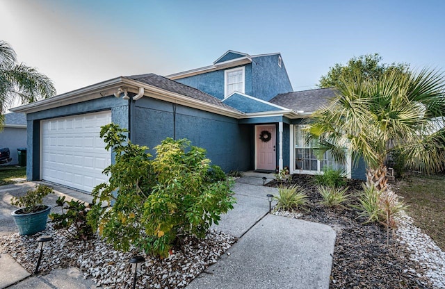 view of front facade with stucco siding, roof with shingles, driveway, and a garage