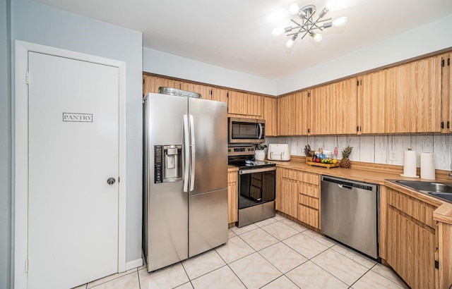 kitchen with a sink, light tile patterned flooring, a notable chandelier, and stainless steel appliances