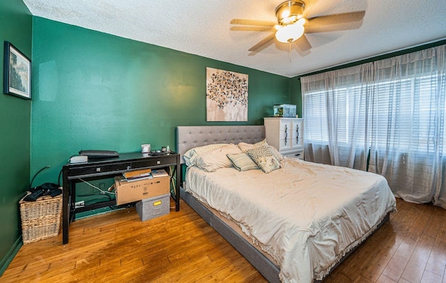 bedroom with a textured ceiling, hardwood / wood-style floors, and a ceiling fan
