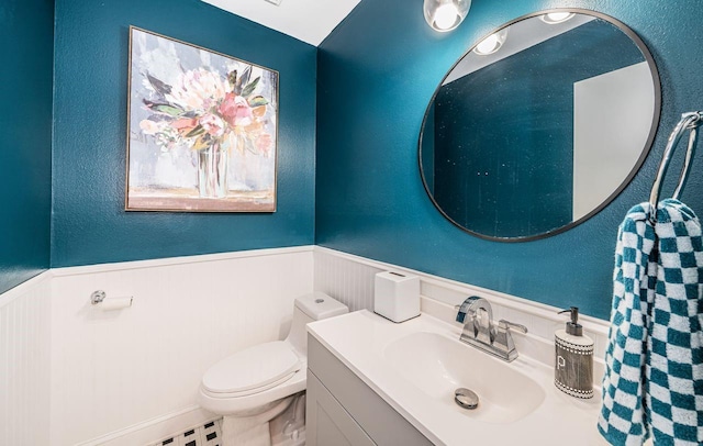 bathroom with a wainscoted wall, toilet, a textured wall, and vanity