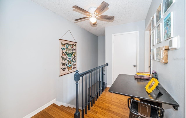stairs featuring a textured ceiling, wood finished floors, a ceiling fan, and baseboards