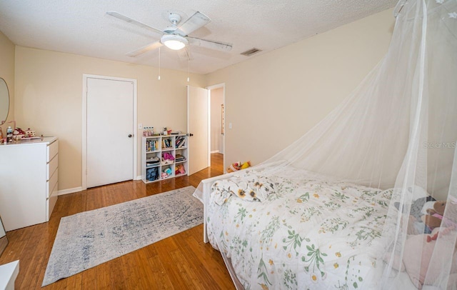 bedroom with a ceiling fan, visible vents, wood finished floors, and a textured ceiling