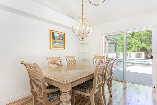 dining space with lofted ceiling, light wood-style flooring, baseboards, and a notable chandelier