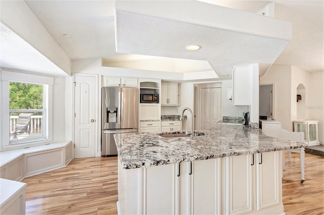 kitchen with built in microwave, light wood finished floors, a sink, a peninsula, and stainless steel fridge