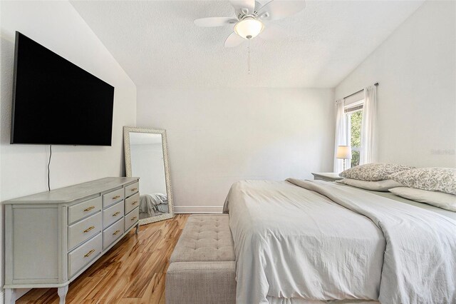 bedroom featuring vaulted ceiling, a ceiling fan, light wood-style floors, baseboards, and a textured ceiling