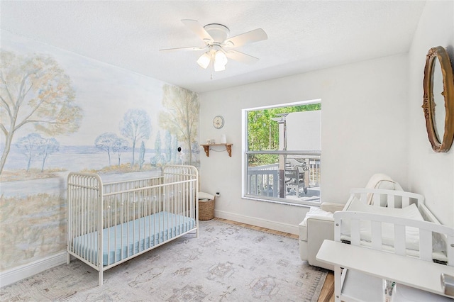 bedroom featuring a ceiling fan, baseboards, a textured ceiling, and a nursery area