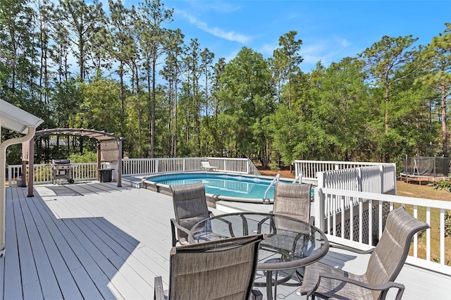 pool with a wooden deck, a trampoline, a pergola, and a grill