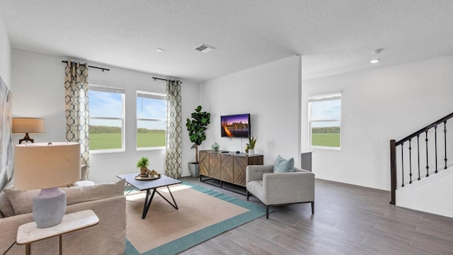 living room featuring wood finished floors, visible vents, stairs, and a healthy amount of sunlight