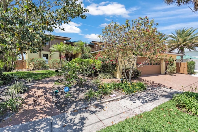 view of property hidden behind natural elements featuring an attached garage, decorative driveway, fence, and stucco siding