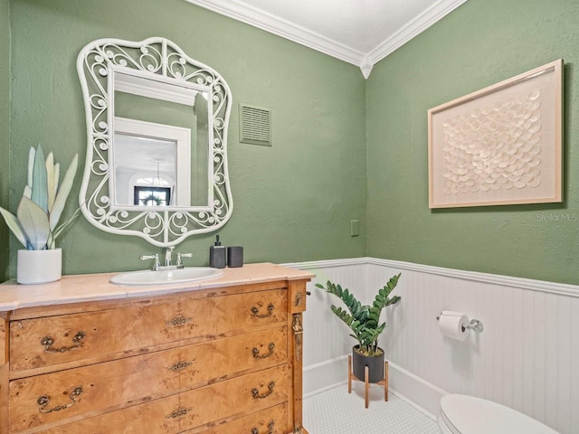 bathroom with wainscoting, ornamental molding, toilet, vanity, and visible vents