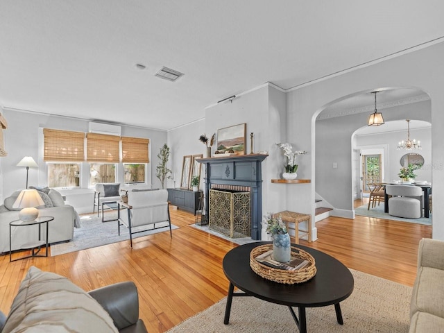 living room with visible vents, arched walkways, ornamental molding, a brick fireplace, and wood finished floors