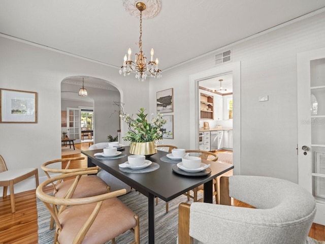 dining space with arched walkways, visible vents, light wood-style flooring, and a chandelier