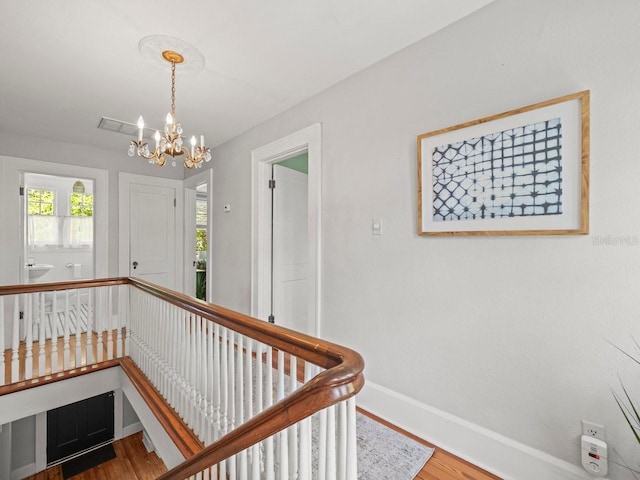 hall with an upstairs landing, wood finished floors, a chandelier, and baseboards