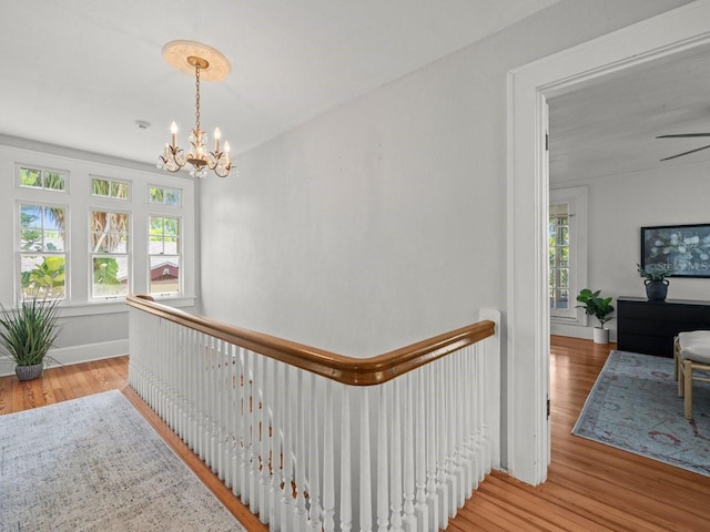 hallway with an upstairs landing, wood finished floors, and a notable chandelier