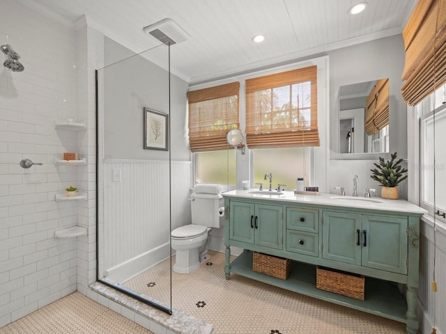 full bathroom with crown molding, a tile shower, double vanity, and a sink