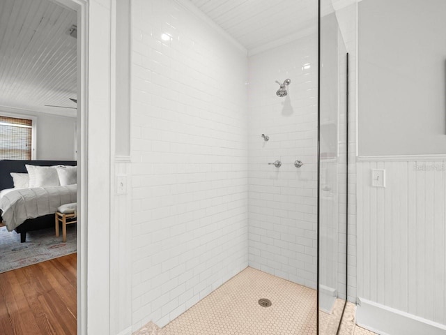 bathroom featuring wood finished floors, a wainscoted wall, and a tile shower