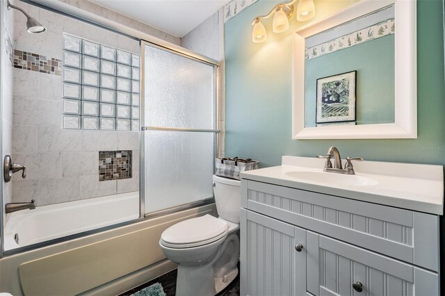 bathroom featuring toilet, bath / shower combo with glass door, and vanity