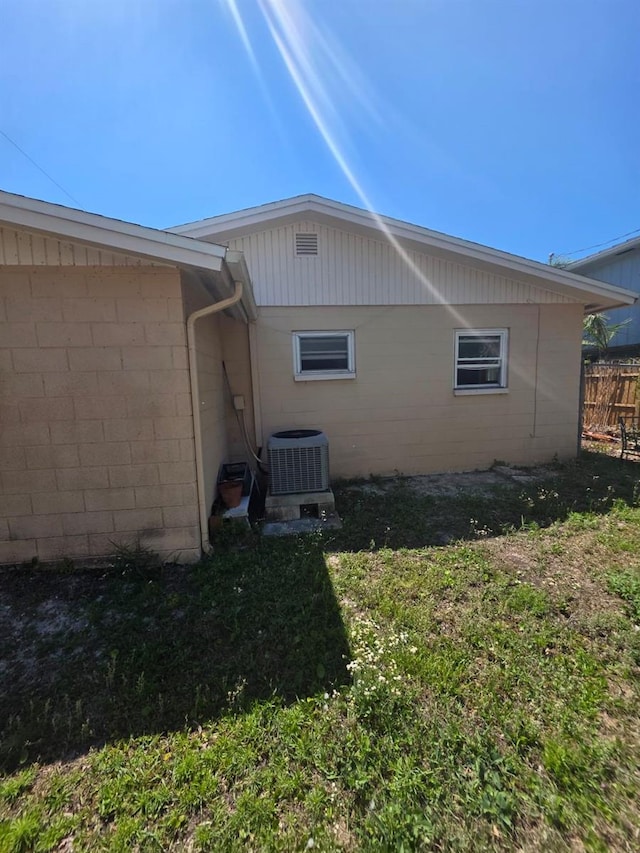 view of side of home featuring fence, concrete block siding, and central AC unit