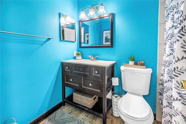 bathroom featuring wood finished floors, toilet, a textured wall, and vanity