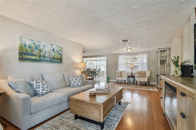 living room featuring a textured ceiling, baseboards, wood finished floors, and visible vents