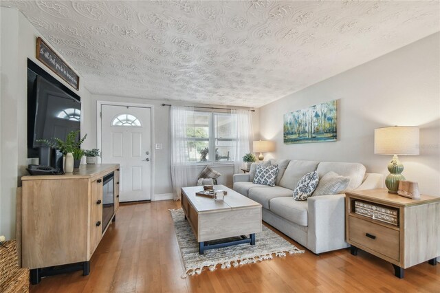 living room featuring a textured ceiling, baseboards, and light wood-style floors