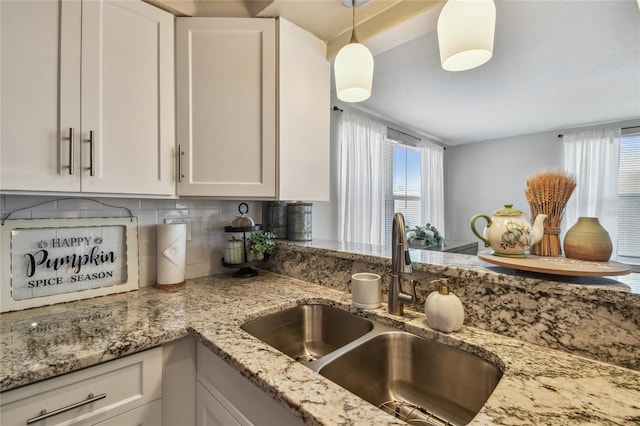 kitchen featuring backsplash, hanging light fixtures, a sink, light stone counters, and white cabinetry