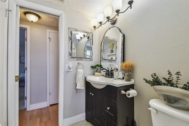 half bathroom with vanity, baseboards, toilet, and wood finished floors