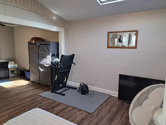 workout room featuring baseboards, wood finished floors, lofted ceiling, and a textured wall