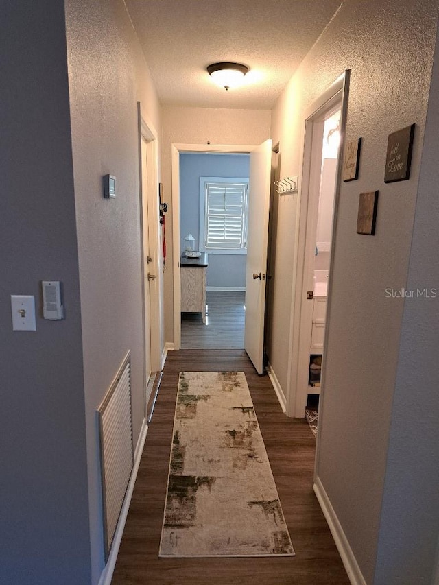 hallway featuring visible vents, baseboards, and dark wood-type flooring