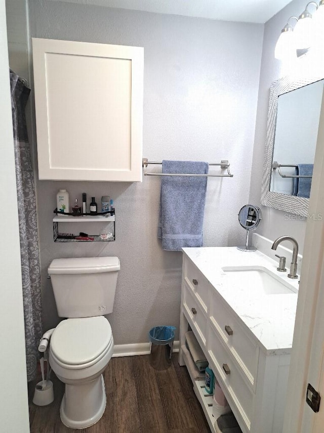 full bathroom featuring baseboards, wood finished floors, toilet, and vanity